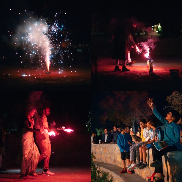 This image is a collage consisting of four photographs taken during a nighttime celebration involving fireworks. The images depict various activities and people, captured under low-light conditions.  Top Left:  A fireworks fountain is lit, emitting a bright burst of colors and sparkles. The sparks and smoke rise vertically, illuminating the surrounding area with a dazzling light. The dark background highlights the vivid colors and intensity of the fireworks. Top Right:  Two people light a firework on the ground. One person is bending down, interacting with the firework that emits a stream of sparks and smoke. The scene is dimly lit, with the glow from the firework providing the primary source of light. Bottom Left:  Two people, possibly a couple, hold a sparkler together. The woman is dressed in traditional attire, and the man is casually dressed. They seem to be enjoying the moment, illuminated by the red glow of the sparkler. Bottom Right:  A group of people, mostly children, are sitting on a low stone wall, watching the festivities. They appear engaged and excited, with some pointing at something in the distance. The background is dark, with the scene primarily lit by ambient light, highlighting their faces and expressions.